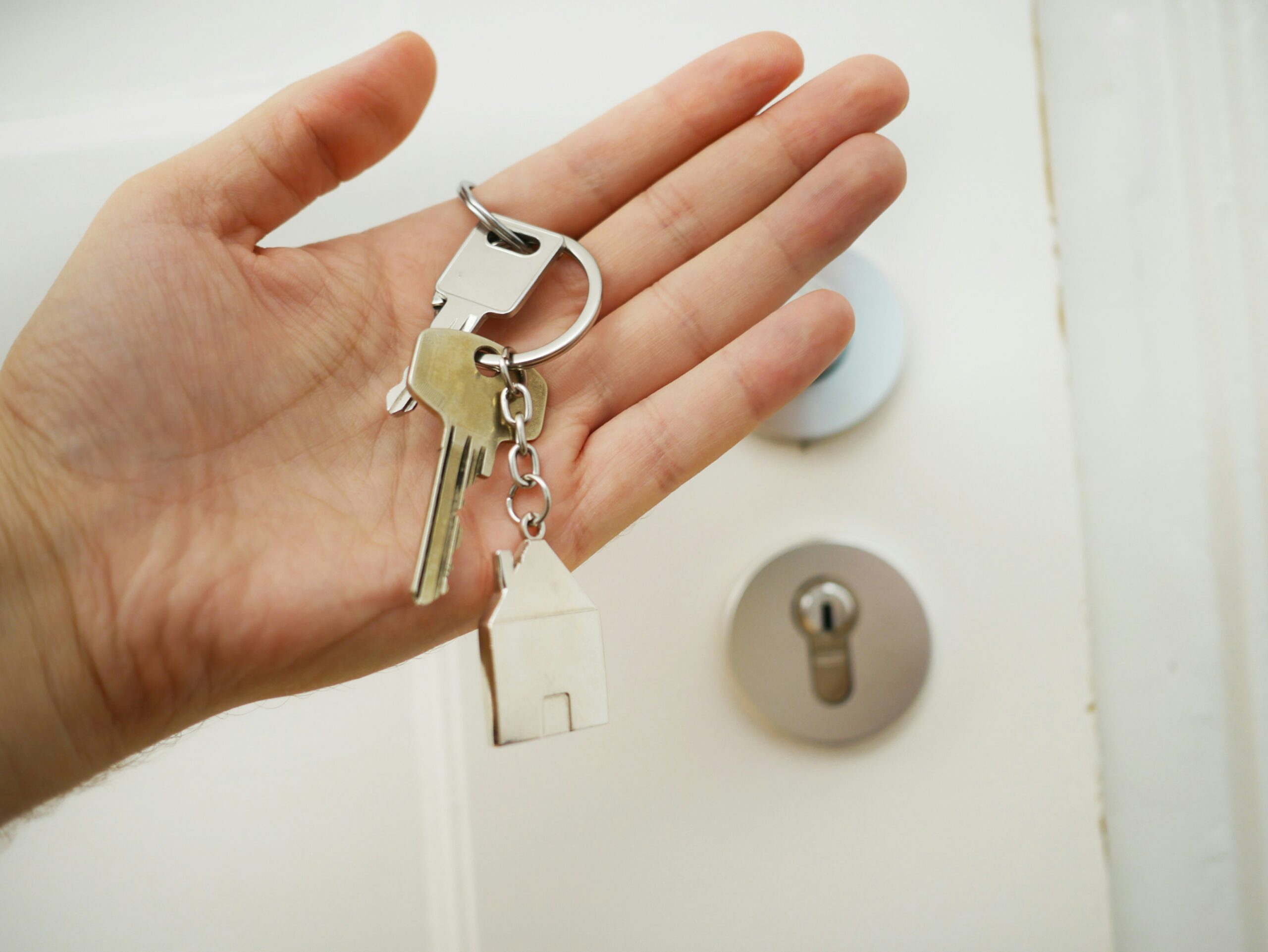 photo of a hand holding house keys in front of a white door, representing the real estate housing market